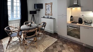 Ett kompakt kök med en matplats, en platt-TV, en modern köksfläkt och en liten arbetsbänk med en kaffemaskin.