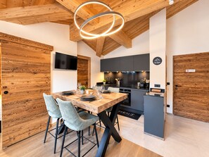 A modern kitchen with a wooden ceiling, a dining table with chairs, and a built-in stove. - Beautiful apartment for 4, Les Gets center, modern and cozy (Les Gets)