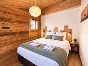 A wooden-paneled room with a bed, a window, and a wall-mounted light fixture.