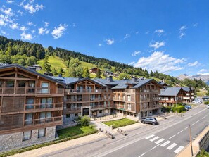 A row of wooden multi-story buildings with balconies, set against a backdrop of a clear blue sky and a hilly landscape.