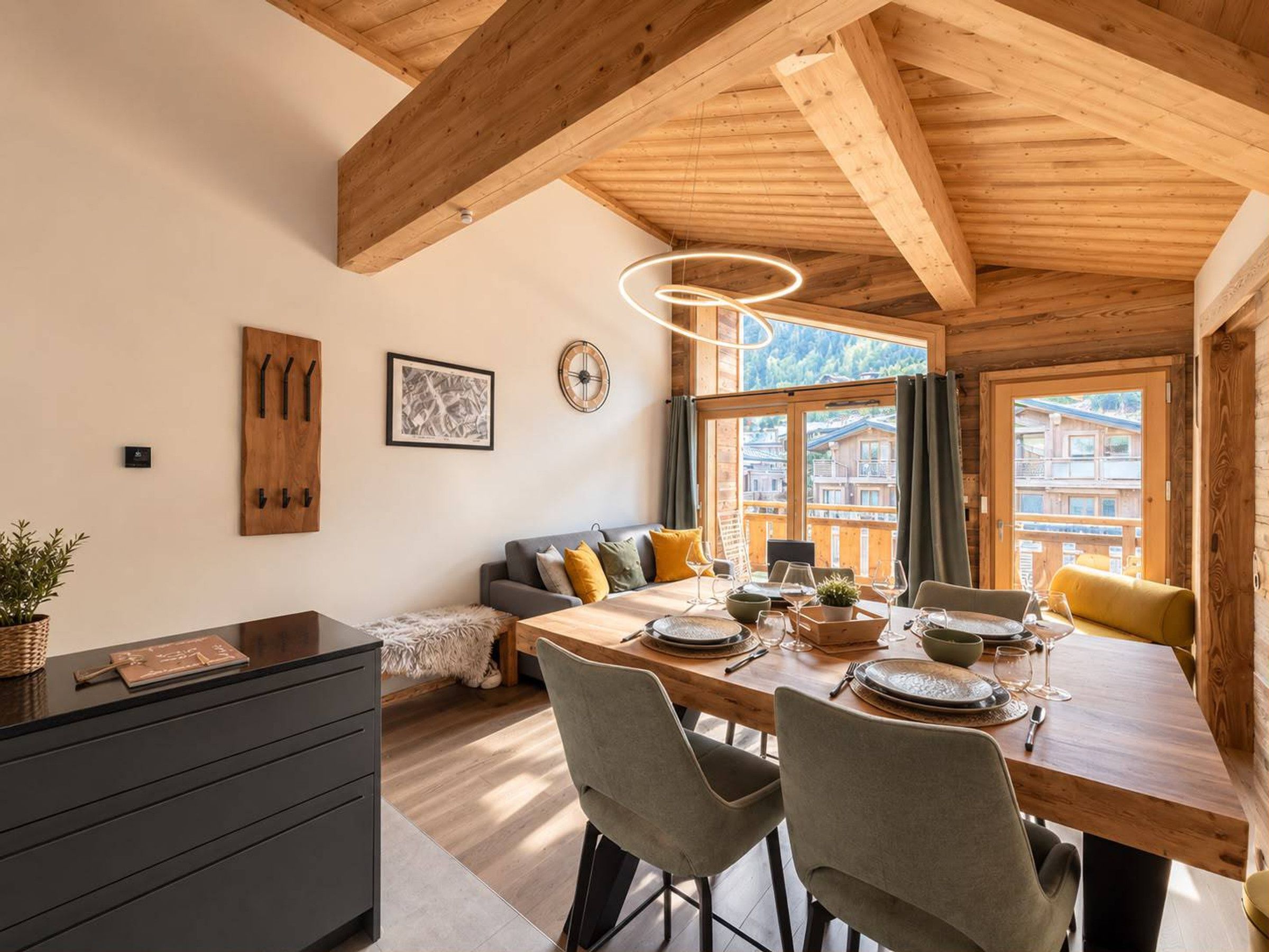 Een houten interieur met een eethoek, een bank en uitzicht op gebouwen.