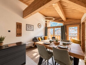 A wooden interior with a dining area, a sofa, and a view of buildings outside. - Beautiful apartment for 4, Les Gets center, modern and cozy (Les Gets)