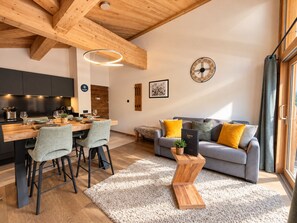 A modern interior with a wooden ceiling, a dining area with a wooden table and chairs, a grey sofa with yellow cushions, and a round wall clock. - Beautiful apartment for 4, Les Gets center, modern and cozy (Les Gets)