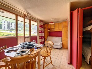 Une pièce compacte comprenant une table à manger pour deux personnes, un lit superposé et une fenêtre donnant sur un bâtiment et sur la verdure environnante.
