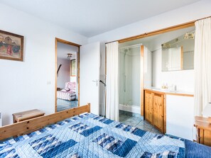 A bedroom with a bed, a wooden nightstand, a bathroom with a shower, and a mirror.