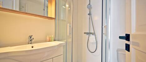 A modern bathroom with a glass-enclosed shower, a white sink, and a mirror above it.