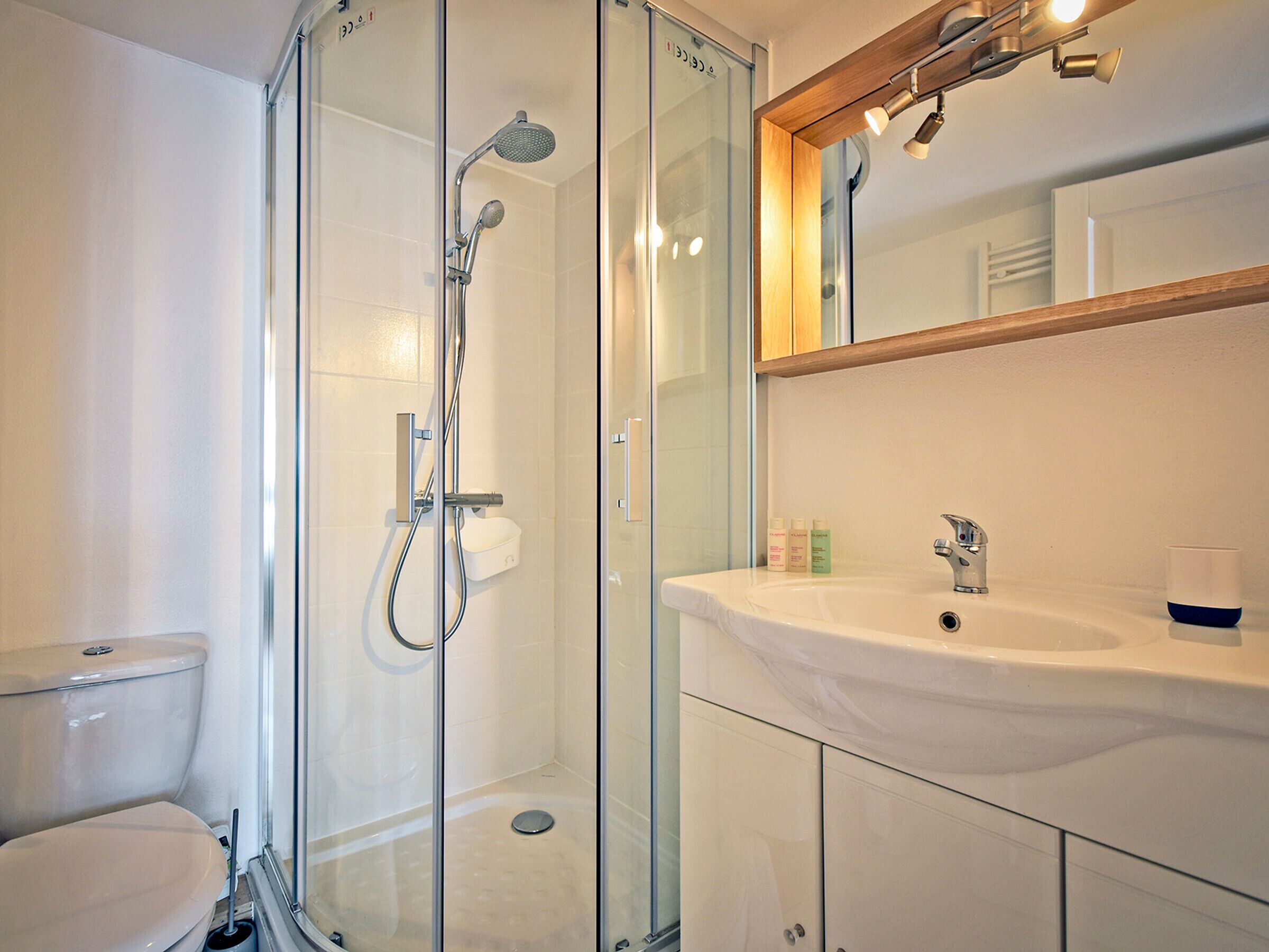 Een moderne badkamer met een douchecabine van glas, een wit wastafelmeubel en een spiegel erboven.