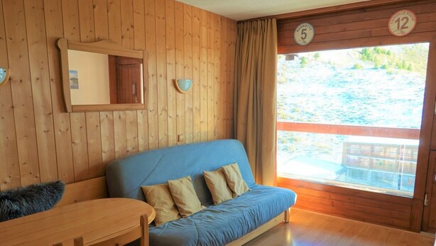 A room with a wooden floor, a blue sofa with cushions, a wooden table, and a window with curtains.
