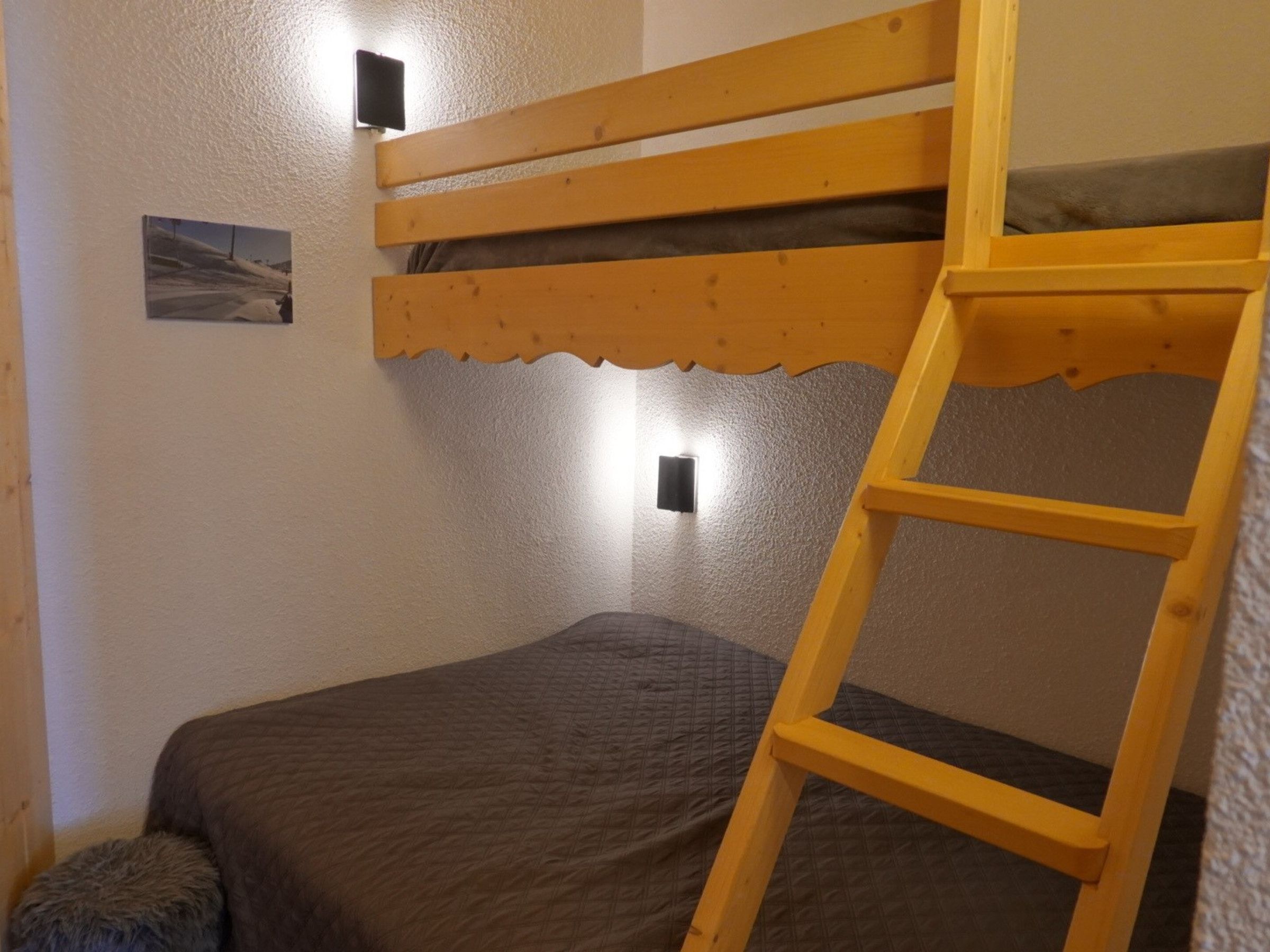 Ein Etagenbett mit einer Stehle, ein kleiner Nachttisch und ein an der Wand befestigtes Regal.