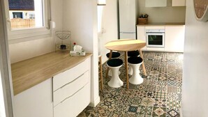 Et kompakt køkken med en træbordplade, et lille spisebord med barstole og et gulv med et mønstret flisegulv.