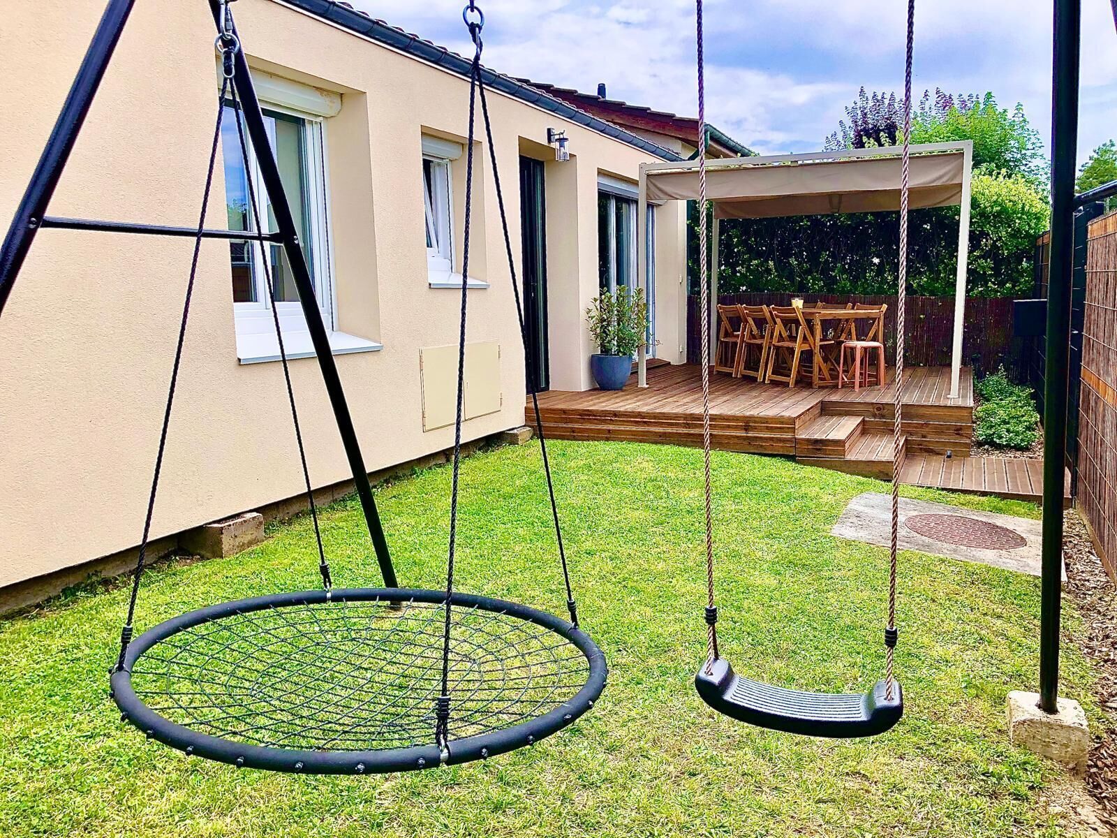 A backyard with a swing set, a covered patio area, and a wooden deck.
