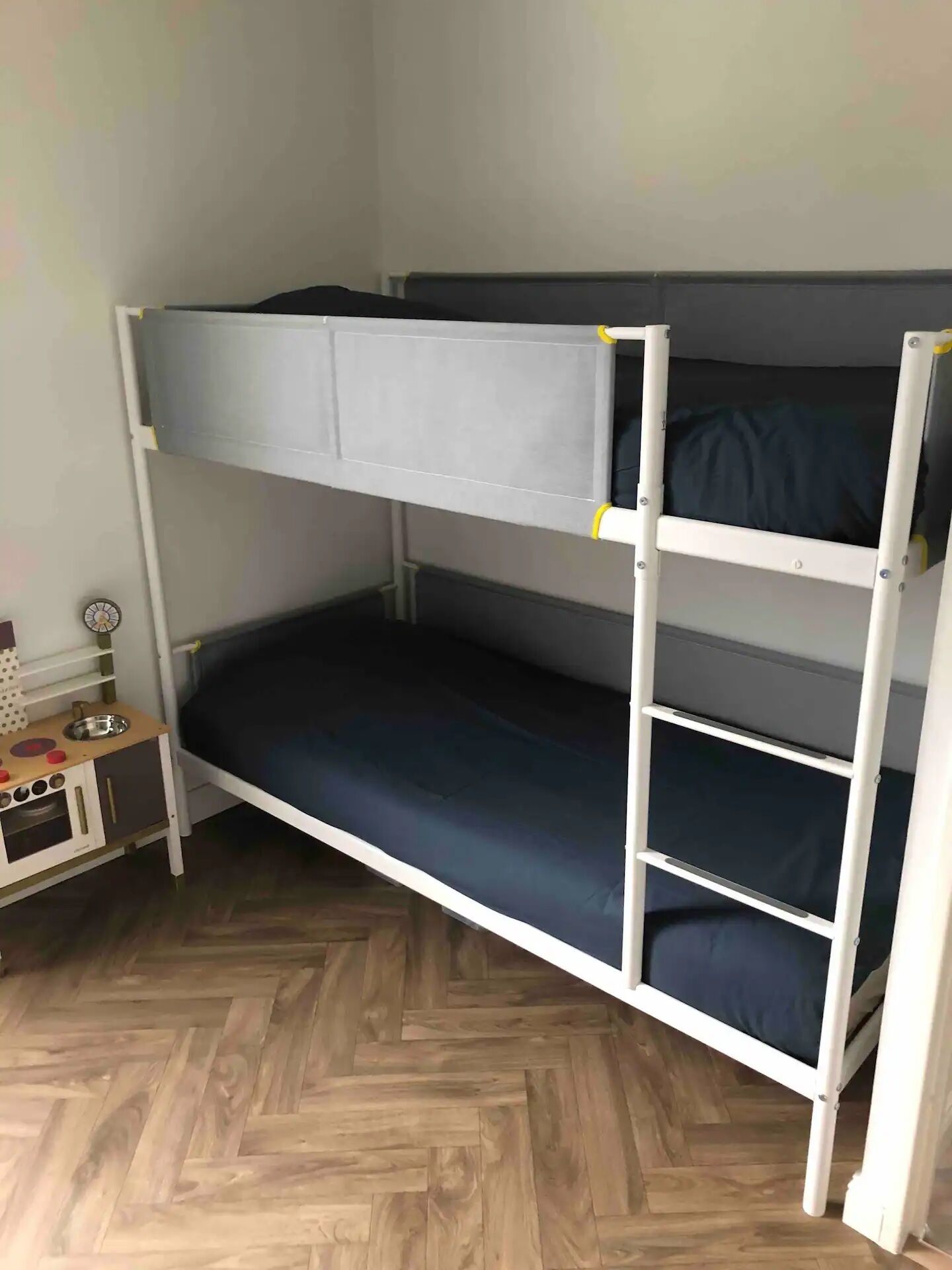 A bunk bed with a desk and chair, a small round table, and a herringbone-patterned floor.