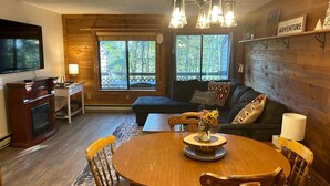 A cozy living room with a wooden dining table, a sofa, and a TV. - Townhouse in Seven Springs: Sleeps 8, Ski, Hike, Swim, Aircon, wifi (Seven Springs)