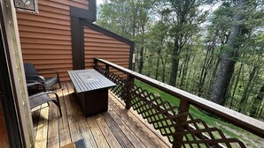 A wooden deck with a table and chairs, a lantern, and a view of a forest. - Townhouse in Seven Springs: Sleeps 8, Ski, Hike, Swim, Aircon, wifi (Seven Springs)