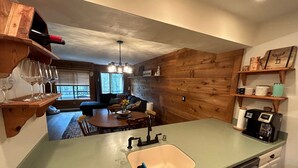 A kitchen with a green countertop, a sink, and a coffee maker. There is a dining area with a table and chairs, and a sofa in the background. - Townhouse in Seven Springs: Sleeps 8, Ski, Hike, Swim, Aircon, wifi (Seven Springs)