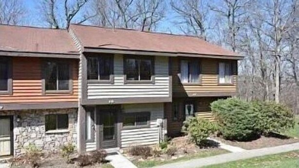 A two-story building with a stone foundation, a wooden front porch, and a small front yard with a bush. - Townhouse in Seven Springs: Sleeps 8, Ski, Hike, Swim, Aircon, wifi (Seven Springs)