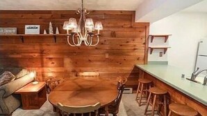 A wooden interior with a dining table surrounded by chairs, a chandelier, and a kitchen area with a sink and stools. - Townhouse in Seven Springs: Sleeps 8, Ski, Hike, Swim, Aircon, wifi (Seven Springs)