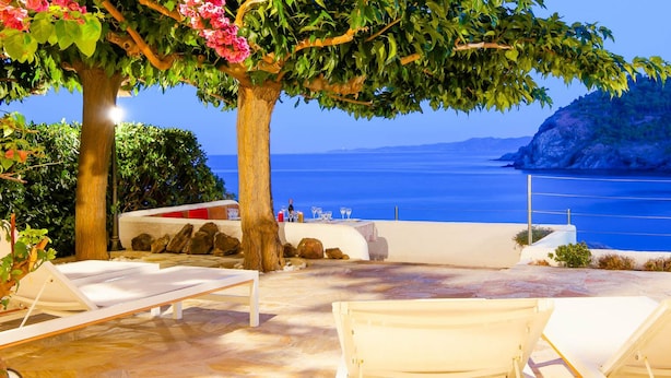 A terrace with white lounge chairs, a table, and a view of the sea.