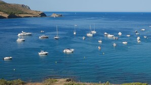 A coastal scene with numerous boats anchored in calm waters, surrounded by rocky terrain and clear skies.