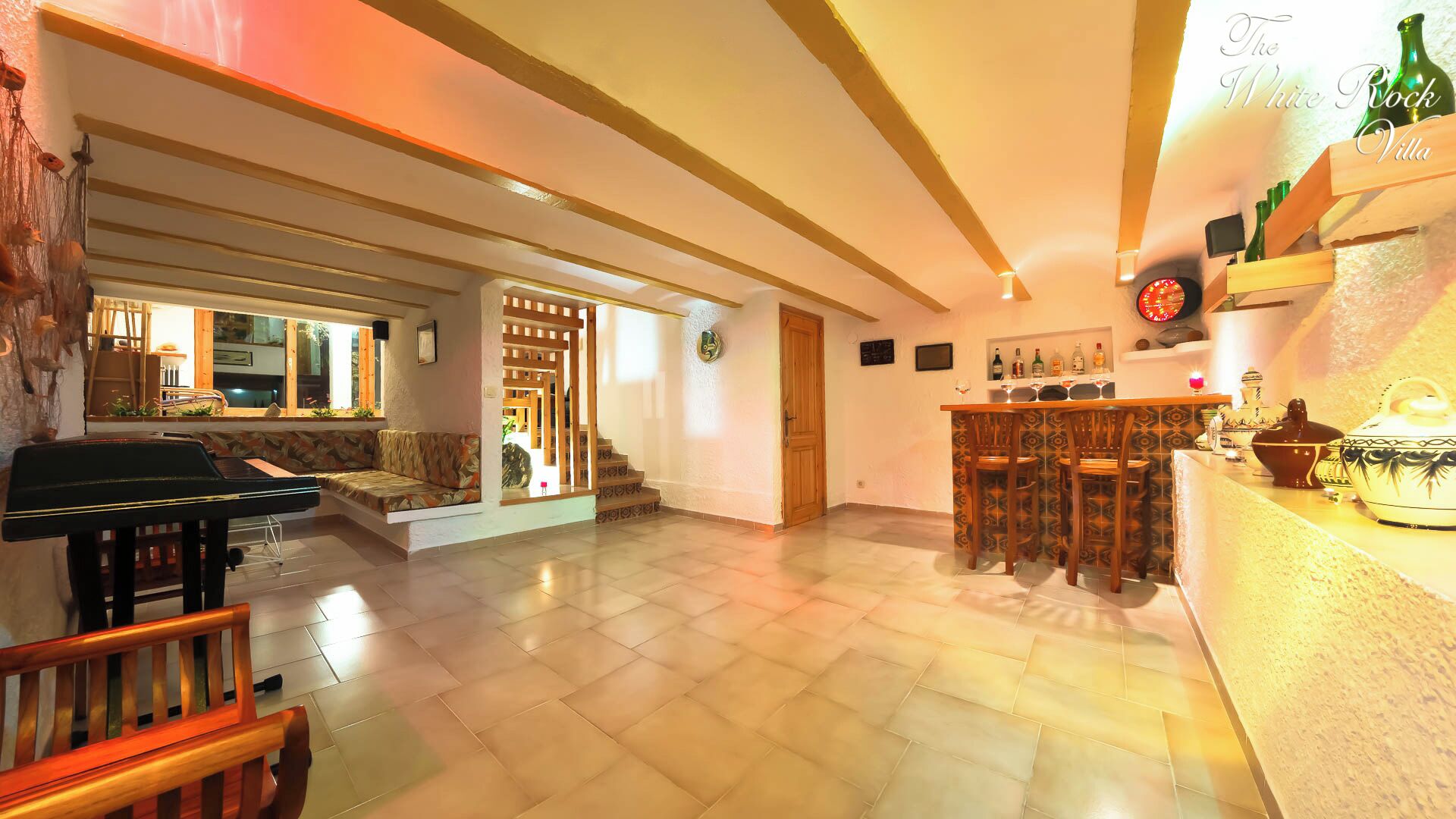 A spacious living area with a piano, a bar area with stools, and a staircase leading to another room.