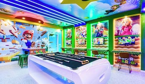Um salão bem iluminado com mesa de bilhar, decora ção temática do Mario e várias telas exibindo jogos de vídeo.