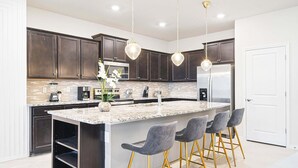 A modern kitchen with dark cabinets, a large island, bar stools, and stainless steel appliances.
