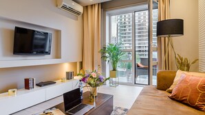 A modern living room with a flat-screen TV mounted on the wall, a laptop on a wooden coffee table, a sofa with cushions, and a large window with curtains. - Lumina platinium Tower Apartments (Warsaw)