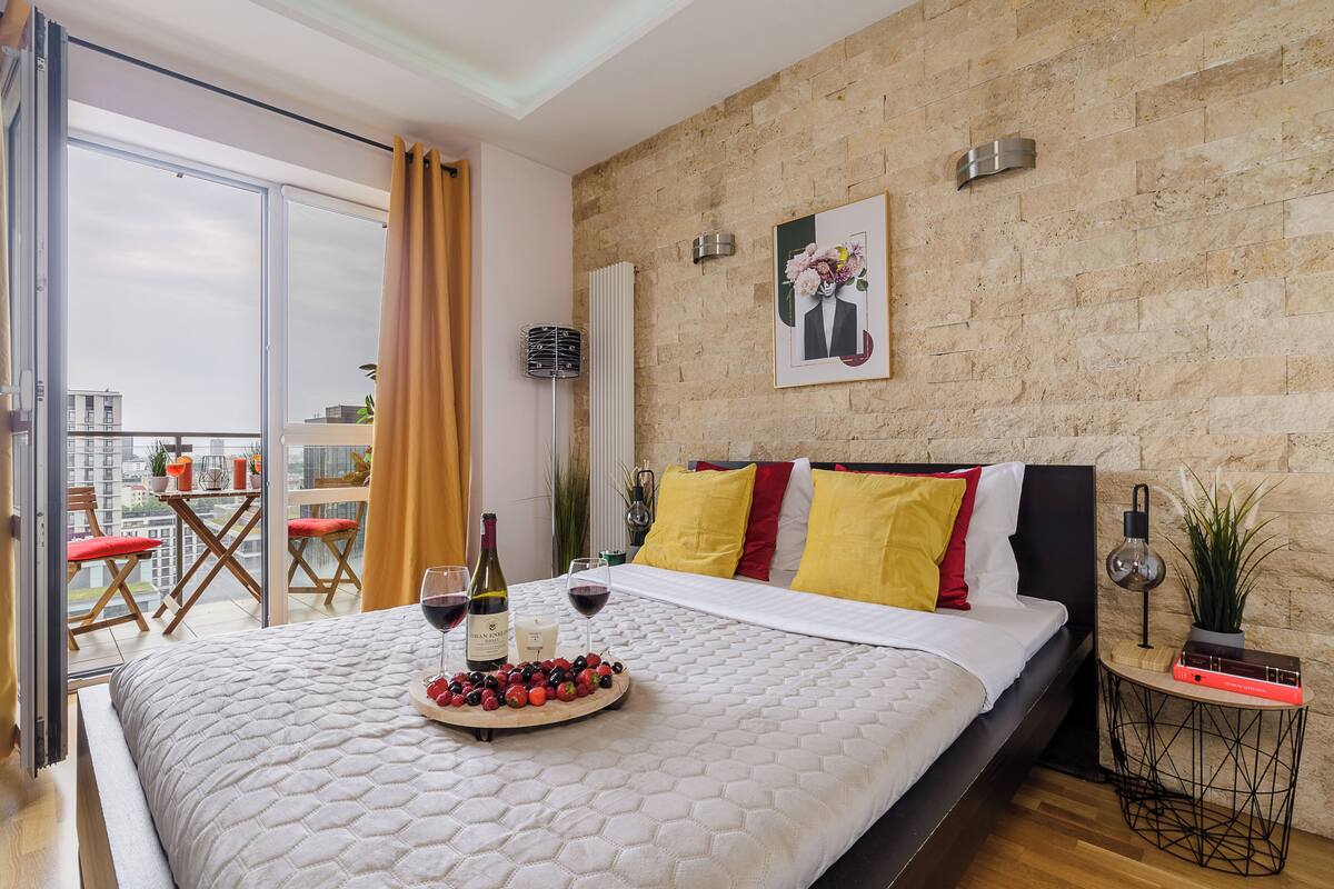 Um quarto com uma cama, uma mesa de cabeceira com luminária, uma obra de arte na parede e vista para a varanda.