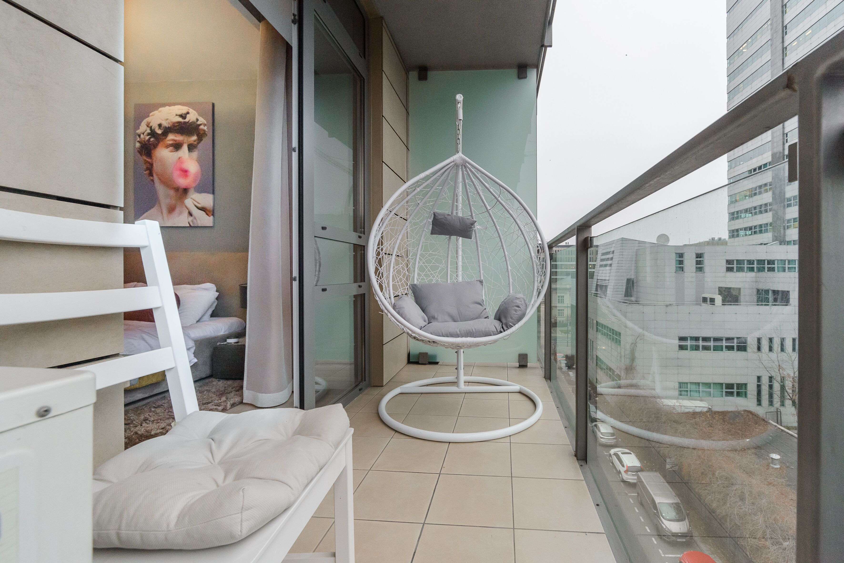 Ein Balkon mit Hängesessel, Sofa und einem Gemälde.