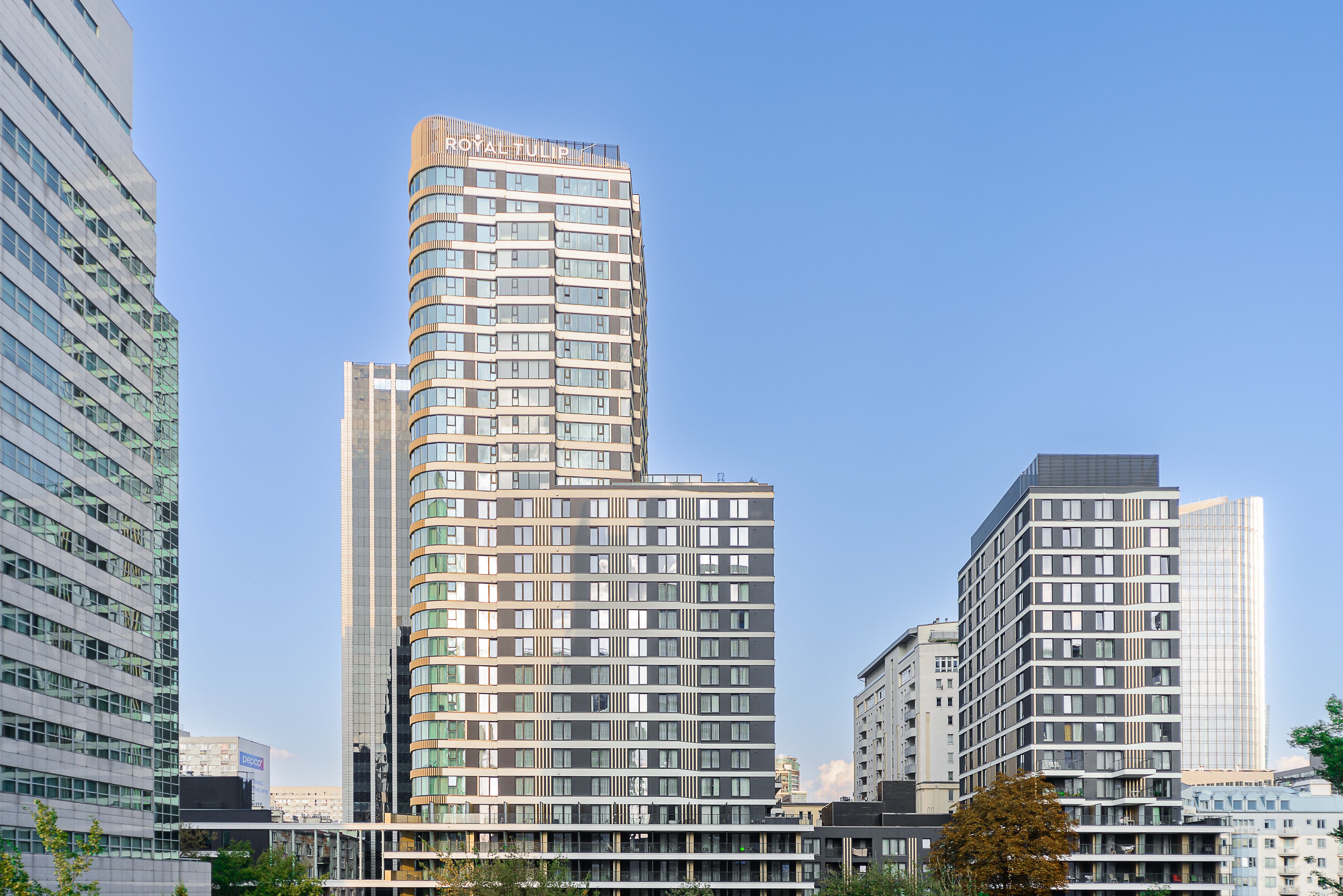 A modern high-rise building with a curved facade, multiple balconies, and a prominent sign at the top.