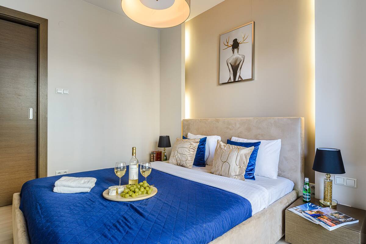 Uma cama bem arrumada com um cobre-leito azul, um prato de uvas, uma garrafa de vinho e uma taça de vinho sobre a cama.