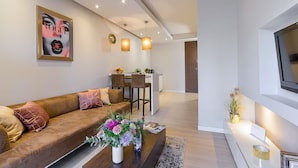 A modern living room with a brown sofa, a coffee table with flowers, and a dining area in the background. - Lumina platinium Tower Apartments (Warsaw)