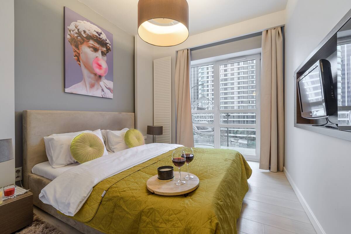 Quarto de hotel moderno com uma cama grande, uma mesa de cabeceira, uma TV e uma janela com vista para a cidade.