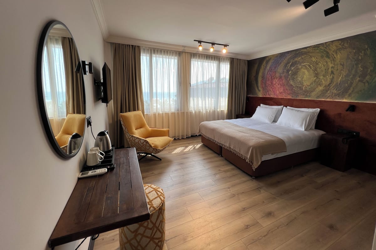 A hotel room with a bed, a desk, a chair, a large mirror, and a painting on the wall.
