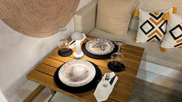 Una mesa de comedor dispuesta con platos, cubiertos y vasos, ubicada en una habitación con un sofá y cojines.
