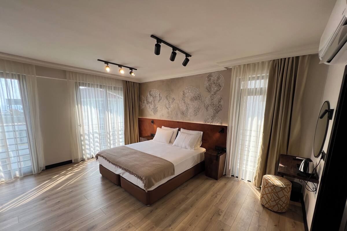 A hotel bedroom with a large bed, wooden flooring, a headboard with wall art, a bedside table, and a mirror.