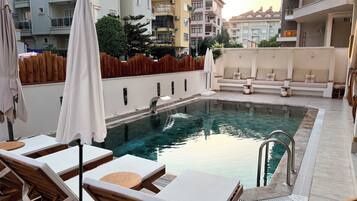 Zona piscina con lettini e una piccola vasca, circondata da palazzi.