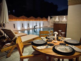 Mesa de comedor preparada para cuatro personas con platos, vasos y cubiertos, con vista a una piscina.