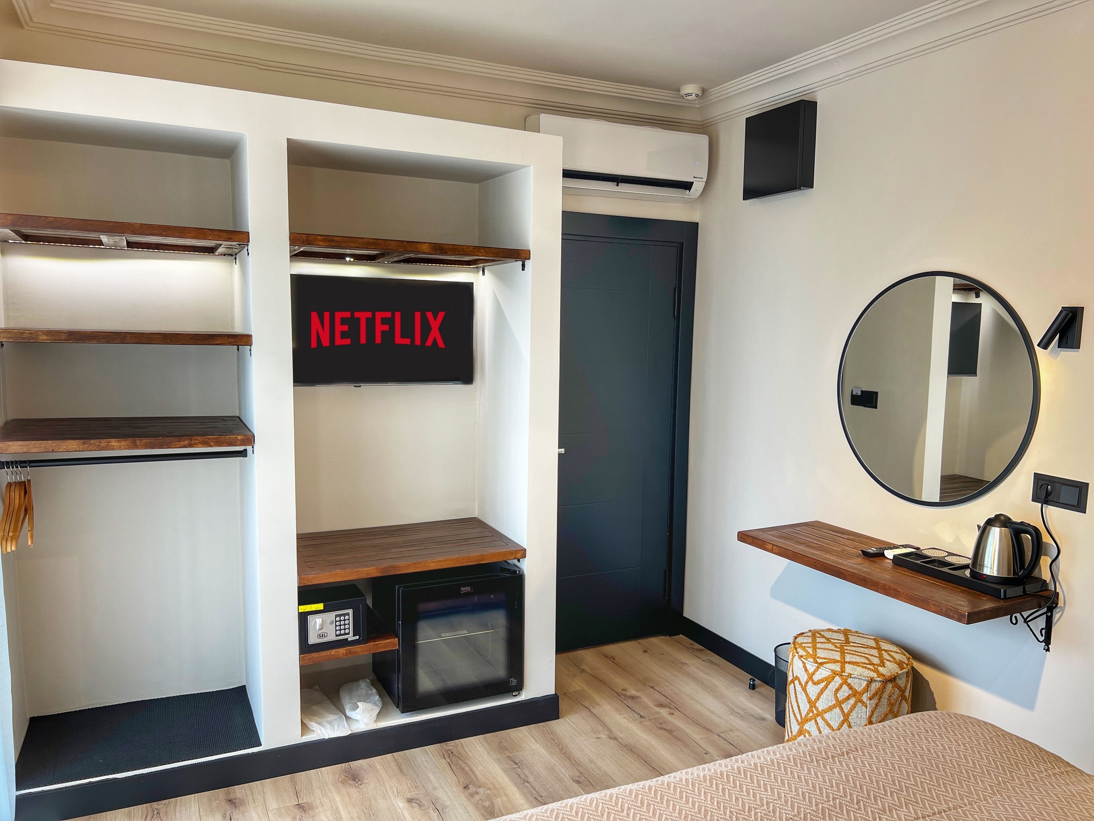 Habitación compacta con horno integrado, una kitchenette pequeña, señal de Netflix, un espejo redondo y un banco de madera.