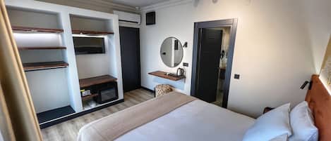 A hotel room with a bed, a desk with a chair, a wardrobe, a mirror, and a door.