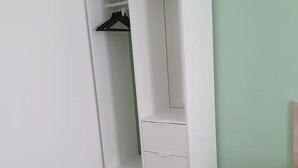 Un armario blanco con varios estantes y cajones, situado frente a una pared verde clara y suelo de madera.