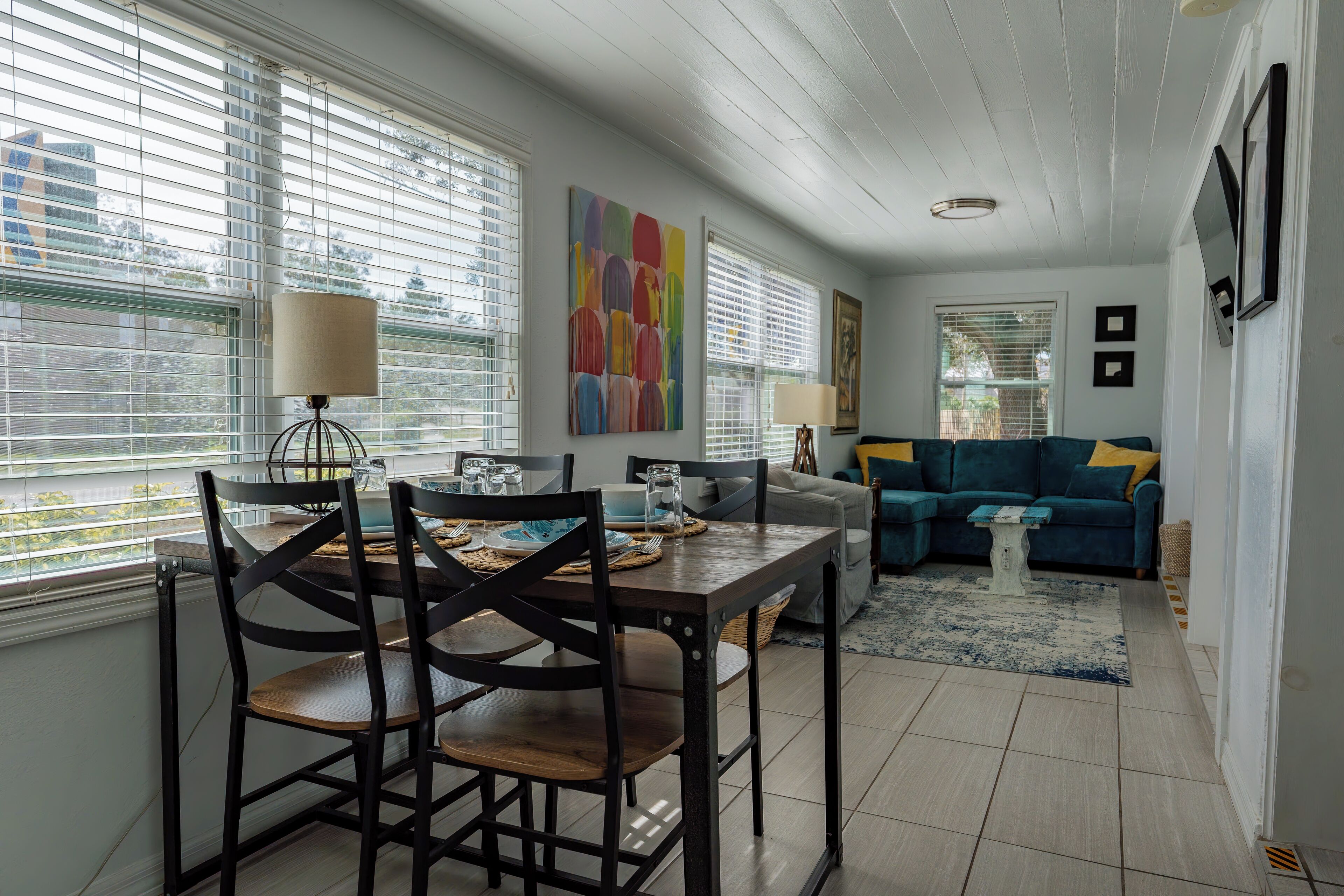 A dining area with a table set for two, a sofa, and a painting on the wall.
