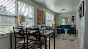 A dining area with a table set for two, a sofa, and a painting on the wall. - Casa Blue - Beautiful Renovated Cottage Close to Downtown! (Safety Harbor)