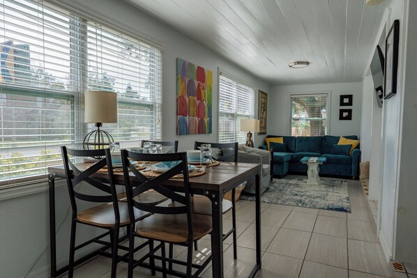 A dining area with a table set for two, a sofa, and a painting on the wall.