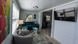 A living room with a blue sofa, a grey armchair, a small coffee table, and a TV on the wall. - Casa Blue - Beautiful Renovated Cottage Close to Downtown! (Safety Harbor)