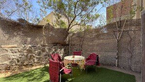 An outdoor patio with a stone wall, a round table, and red chairs. - 98. Homey 2BR Townhouse | 2 Queen Beds | Garden (Sheikh Zayed City)