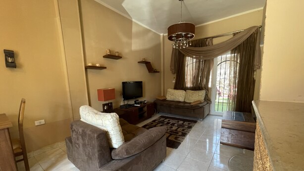 A living room with a sofa, TV, and a chandelier. - 98. Homey 2BR Townhouse | 2 Queen Beds | Garden (Sheikh Zayed City)