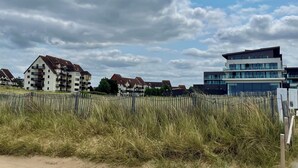 Un quartier résidentiel en bord de mer, avec des immeubles modernes, une clôture en bois et des dunes herbeuses.