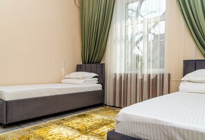 Une chambre d’hôtel avec deux lits, une grande fenêtre avec des rideaux légers et une moquette à motifs.