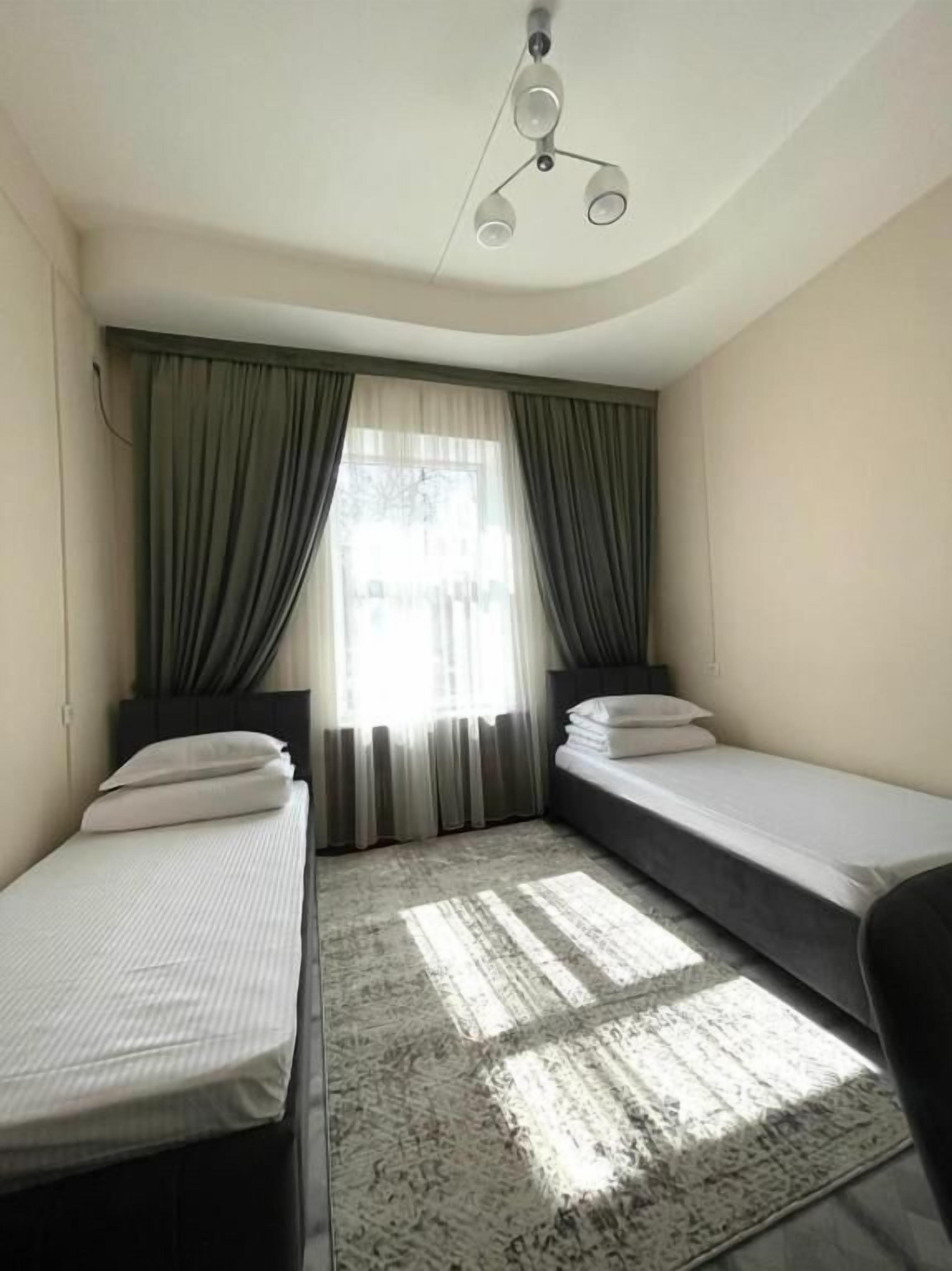 Una habitación pequeña y moderna con dos camas individuales, un ventilador de techo y un gran ventanal con cortinas.